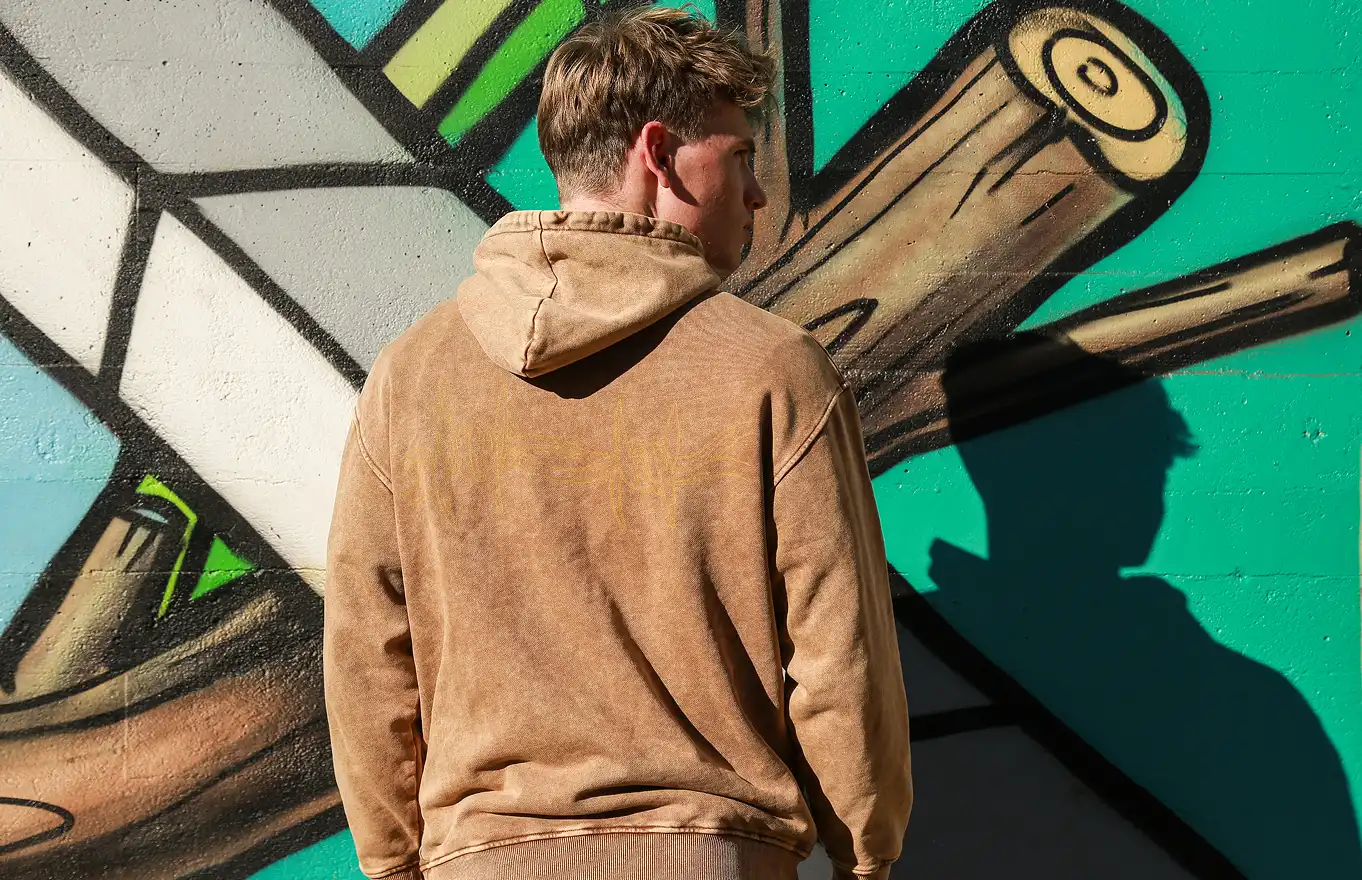 The man is showcasing a high-quality hoodie with tapstitch design under the sunlight.